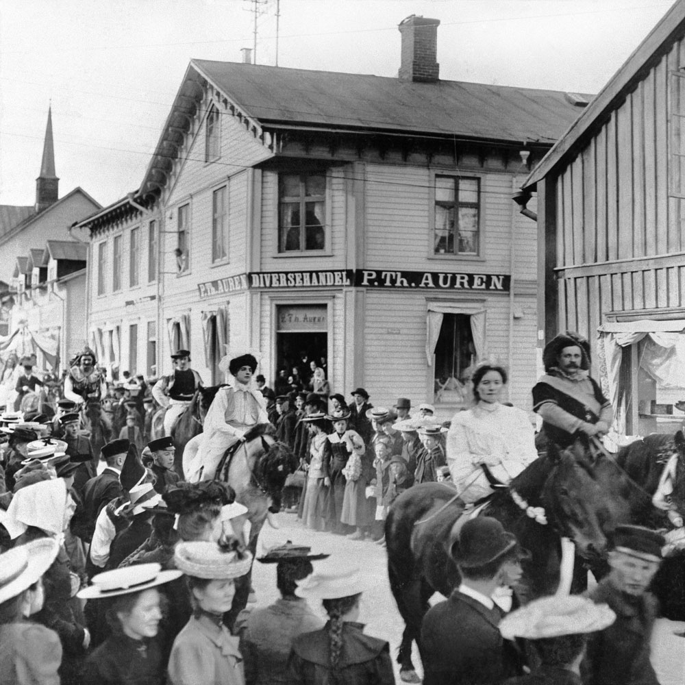 Ridande procession genom staden, stor folksamling.