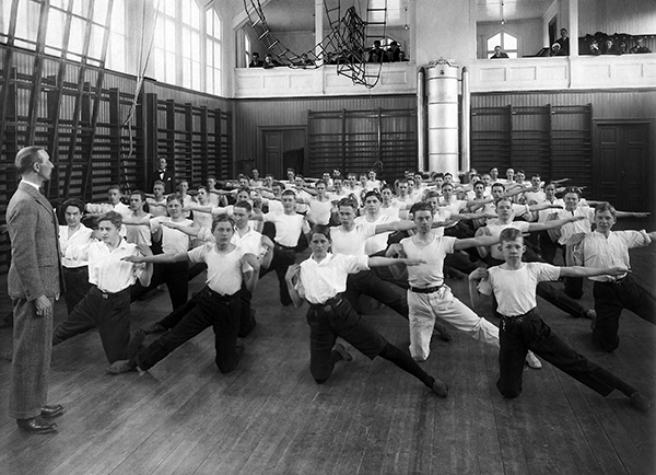 Gymnastiksal med knästående pojkar som sträcker ut armen åt sidan.