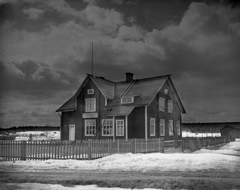 Skolbyggnad av trä i två våningar och med skylt som det står Skolhus på.